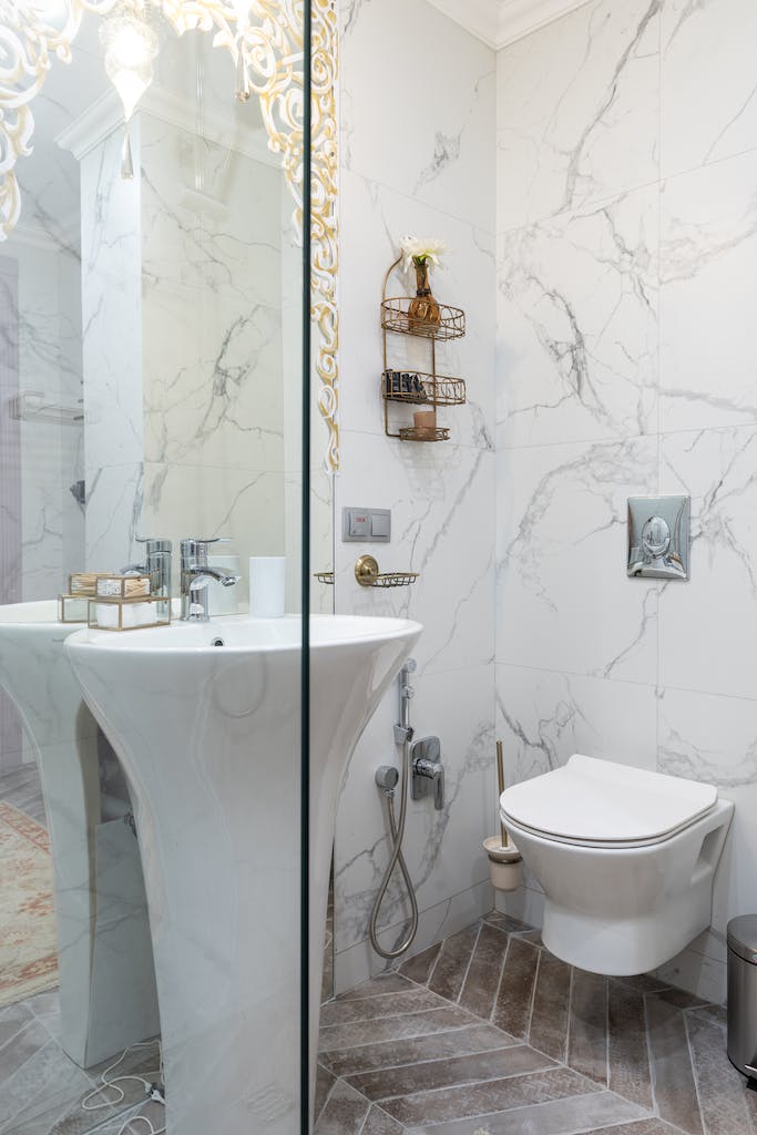 Interior of stylish restroom with white sink placed between glass transparent shower cabin and bidet at tiled wall at home